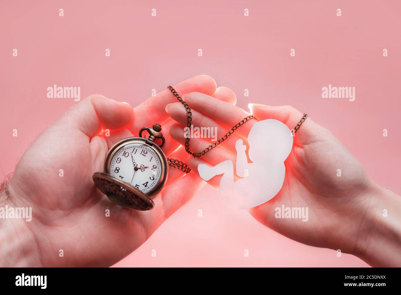 Hands of woman and man holding a silhouette of a child and clock. Paper silhouette and time before the birth of the child Stock Photo