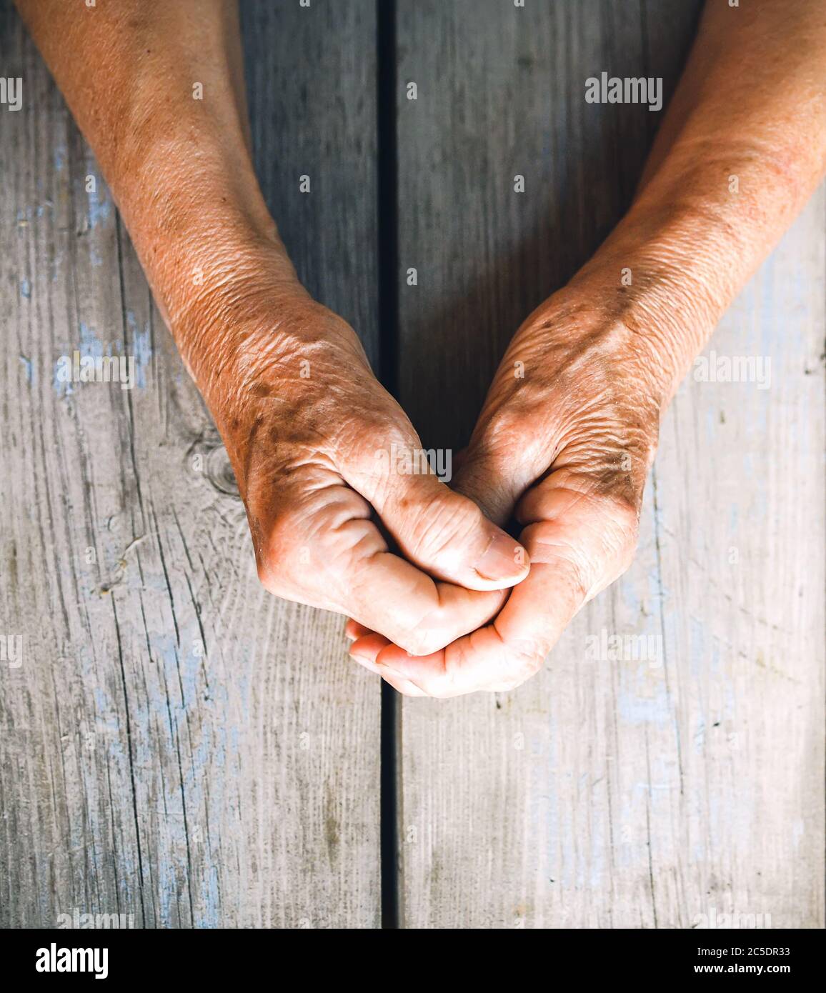 Elderly woman hands on rustic wooden background. Senior woman with fingers crossed. Wrinkled palms stretched forward. Religion, take care, mothers day Stock Photo