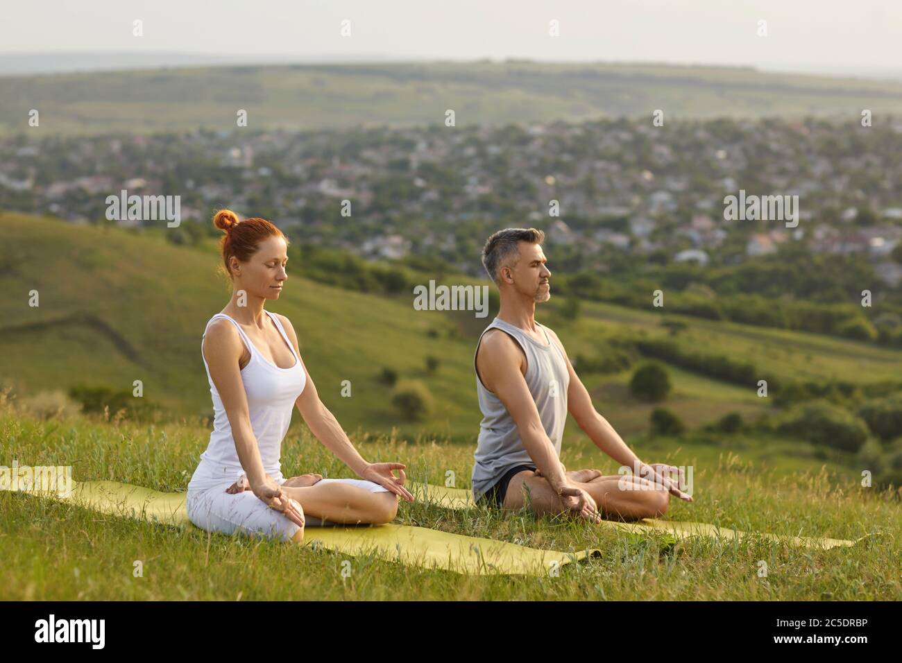 Yoga in nature. Millennial couple doing yoga meditation in mountains. Man and woman practicing breath exercises outdoors Stock Photo