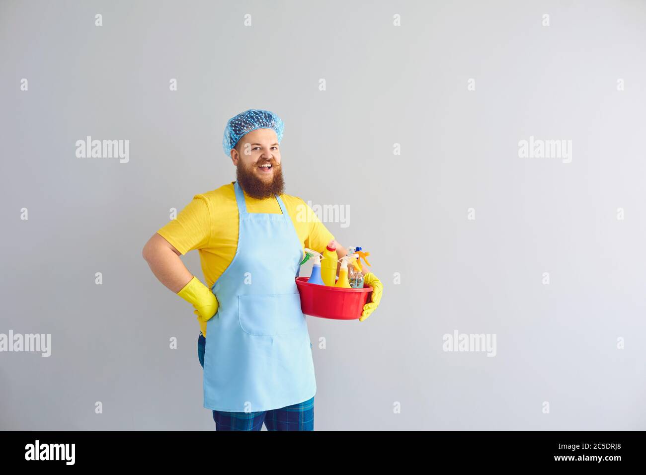 Funny fat guy with cleaning supplies on grey background, copy space. Sanitary service worker doing house chores Stock Photo
