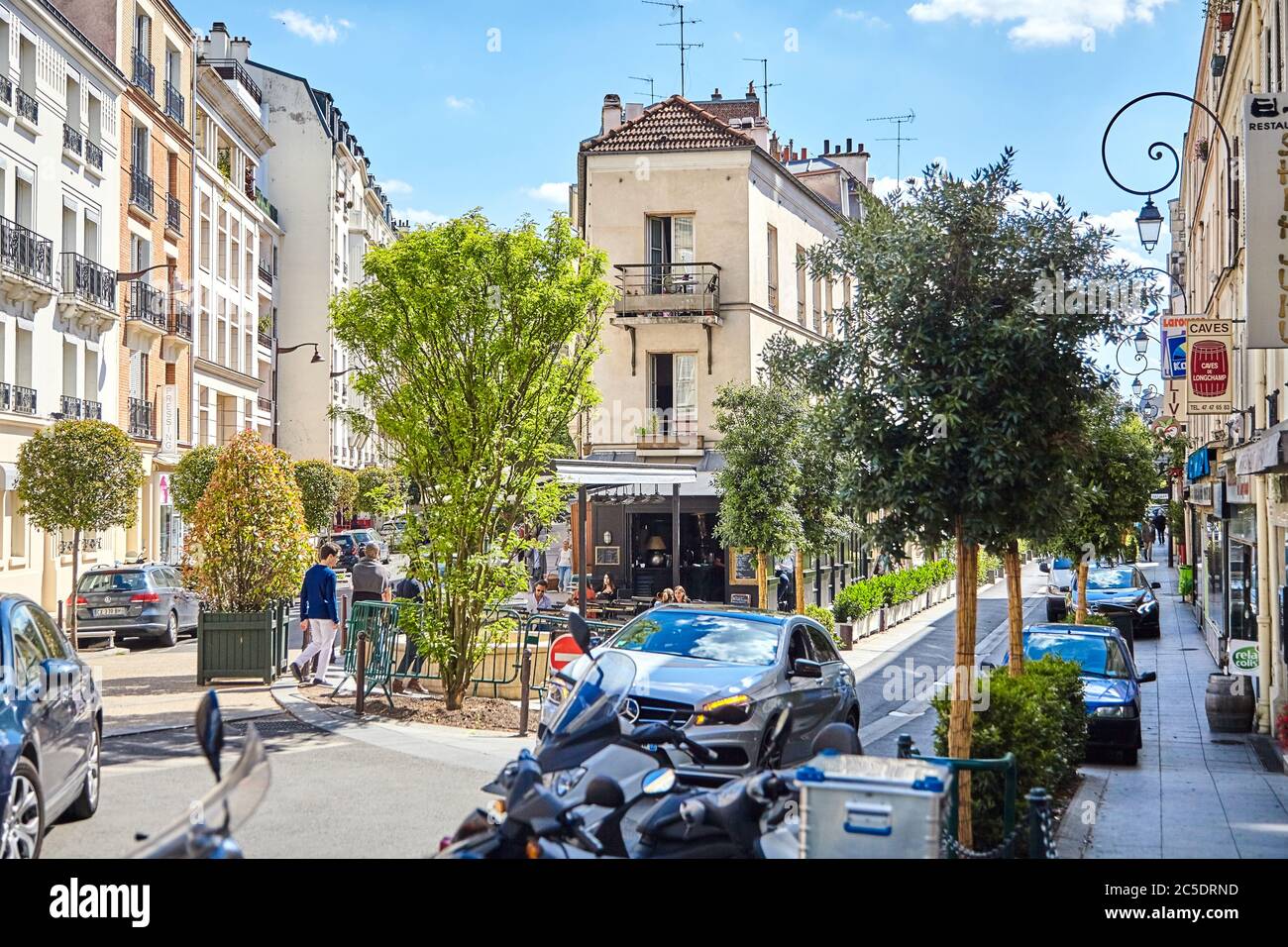 Paris, France - June 19, 2015: Parked cars in the narrow cozy streets of the city. Cafe on the corner of a house among green trees Stock Photo