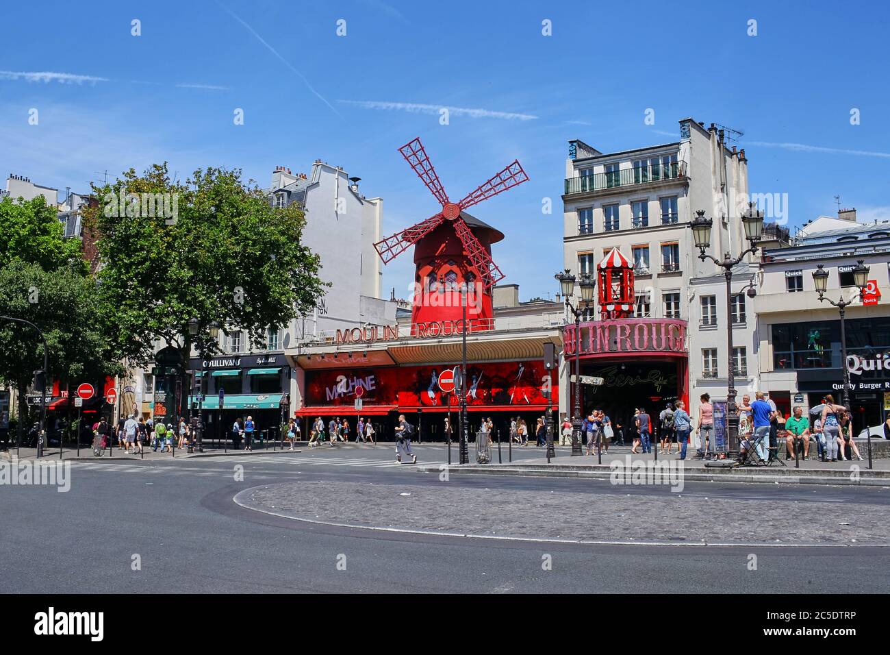 Paris, France - June 28, 2015: Moulin Rouge is a famous cabaret in the city. The red light district of Pigalle. People walking along the sidewalk. Sum Stock Photo