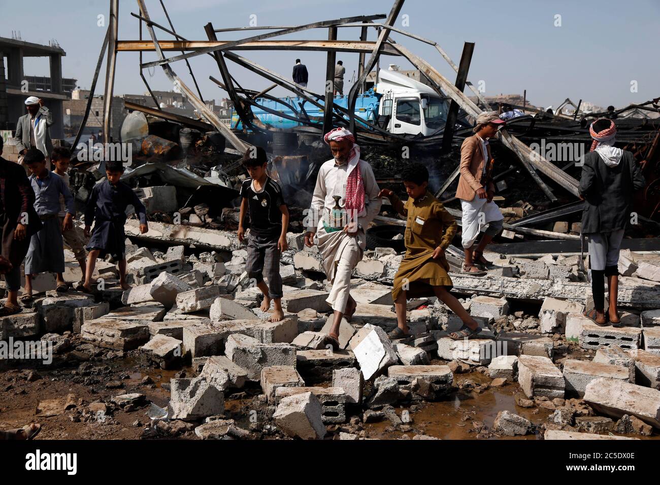 Sanaa, Yemen. 2nd July, 2020. Yemeni people walk on the rubble of a warehouse after it was hit by airstrikes in Sanaa, Yemen, on July 2, 2020. The Saudi-led coalition on Wednesday launched a series of airstrikes on the Yemeni capital Sanaa, which is under Houthi control, the Houthi-run al-Masirah TV reported. Credit: Mohammed Mohammed/Xinhua/Alamy Live News Stock Photo