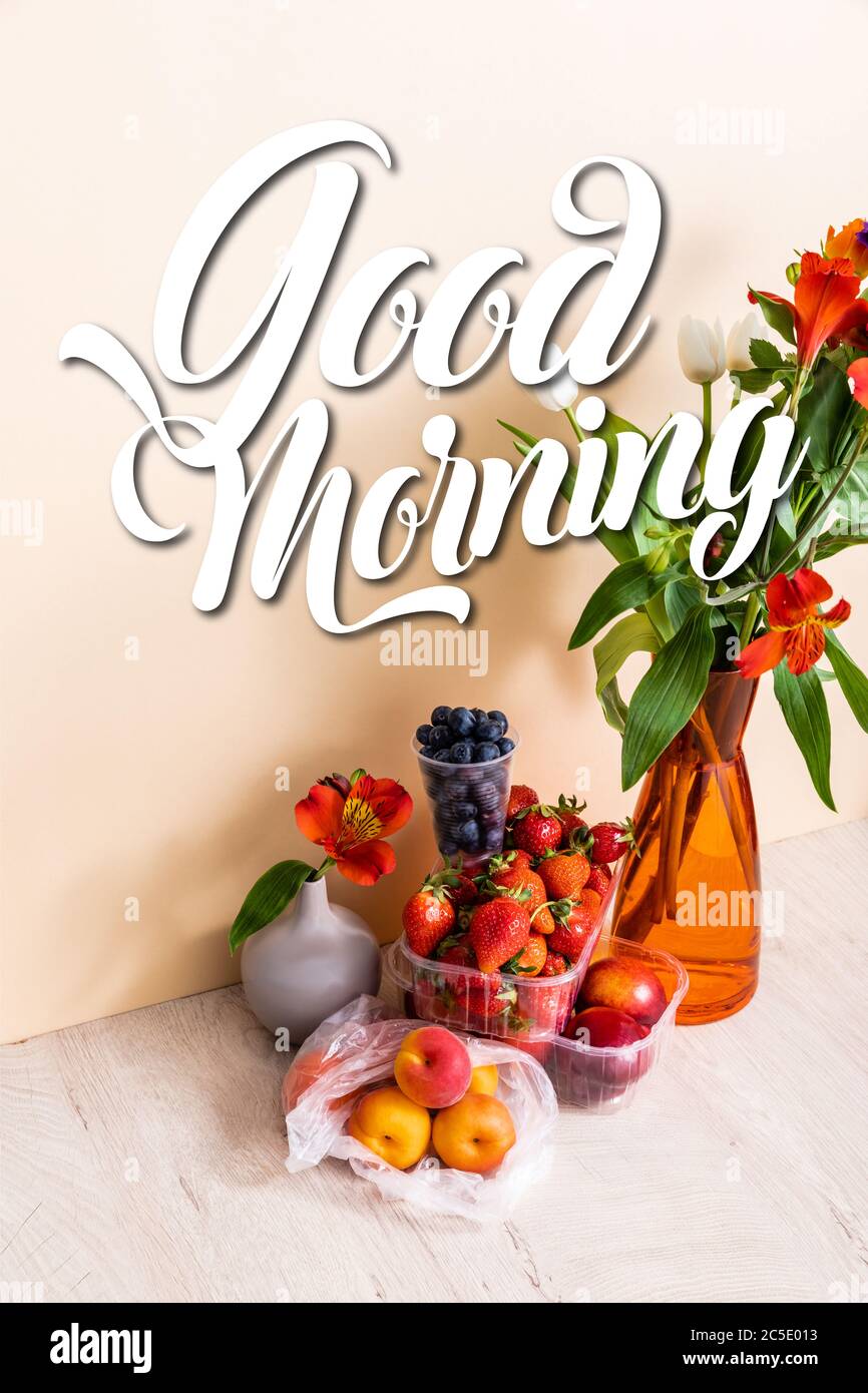 floral composition with flowers in vases near fruits and good morning lettering on beige Stock Photo