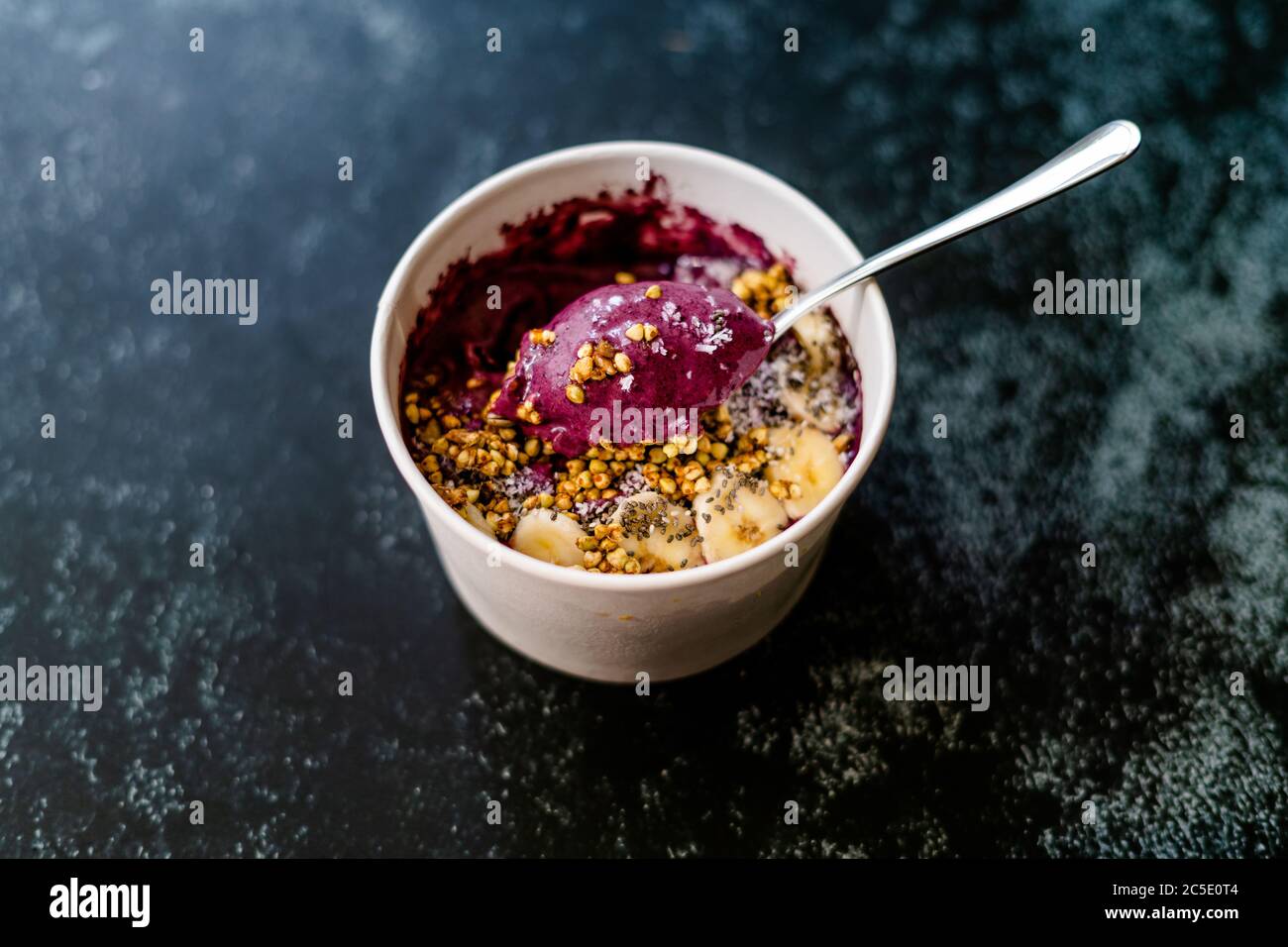 Take Away Vegan Food Acai Bowl with Almond Milk, Peanut Butter, Banana, Buckwheat Granola, Chia Seeds and Chocolate Pieces in Carton Bowl. Healthy Org Stock Photo