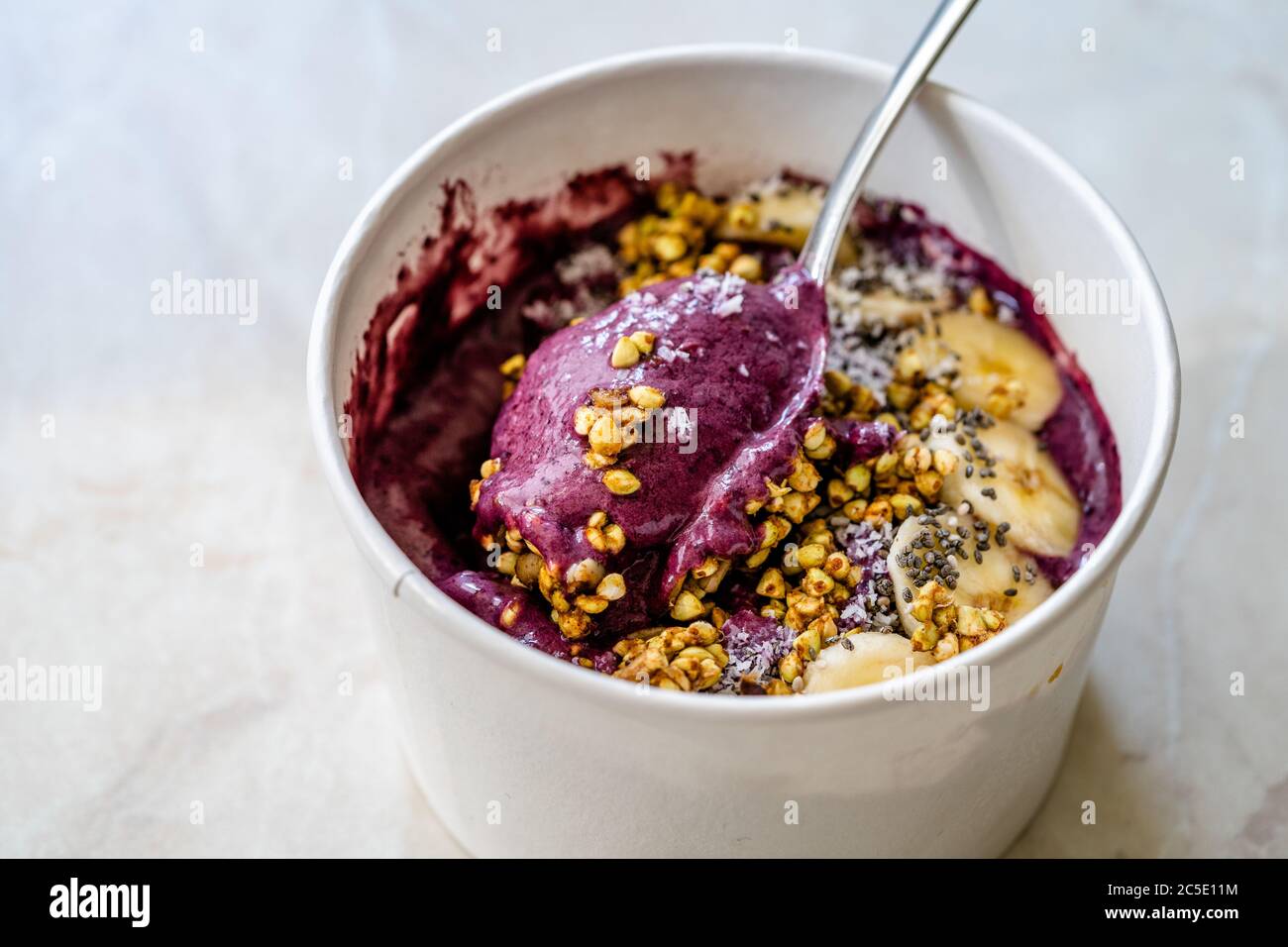 Take Away Vegan Food Acai Bowl with Almond Milk, Peanut Butter, Banana, Buckwheat Granola, Chia Seeds and Chocolate Pieces in Carton Bowl. Healthy Org Stock Photo