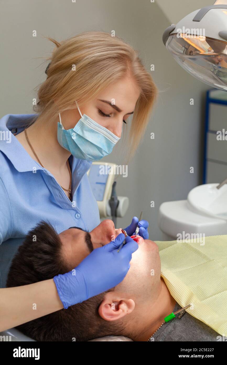 Man visiting female dentist at clinic. Young man sitting mouth wide
