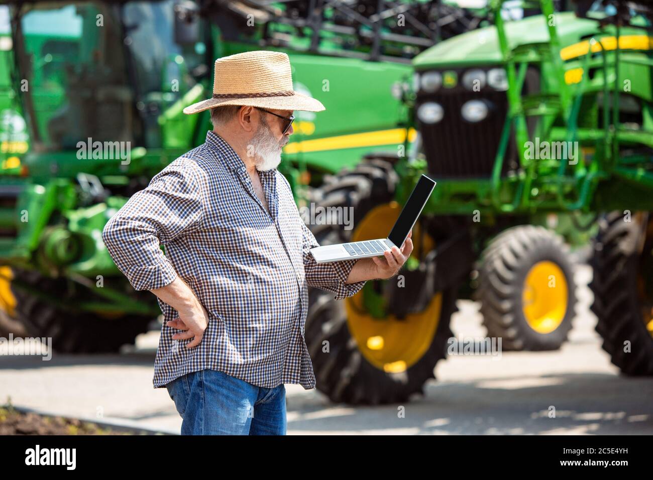 Professional farmer with a modern tractor at work with laptop. Looks ...