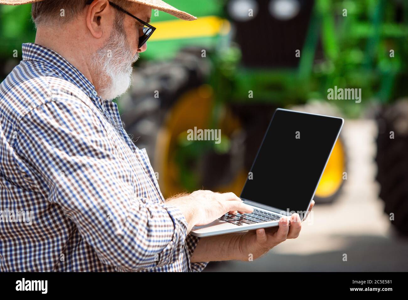 Professional farmer with a modern tractor at work with laptop. Looks ...