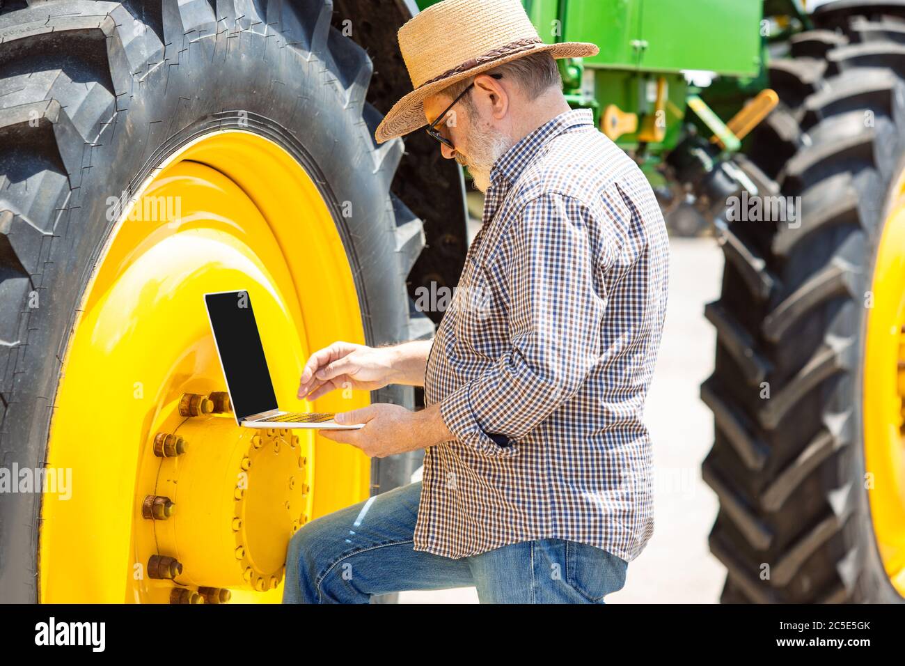 Professional farmer with a modern tractor at work with laptop. Looks ...