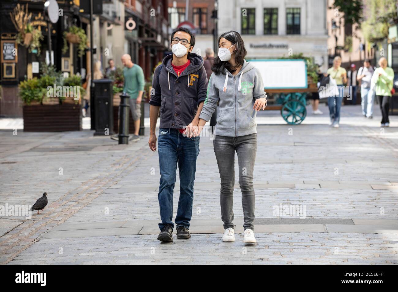 Covent Garden, London, UK/ 2nd July 2020. A couple wearing face masks walk along the piazza in Covent garden before Super Saturday ahead of the coronavirus lockdown restrictions being relaxed and restaurants and bars open this weekend across London, UK Credit: Clickpics/Alamy Live News Stock Photo