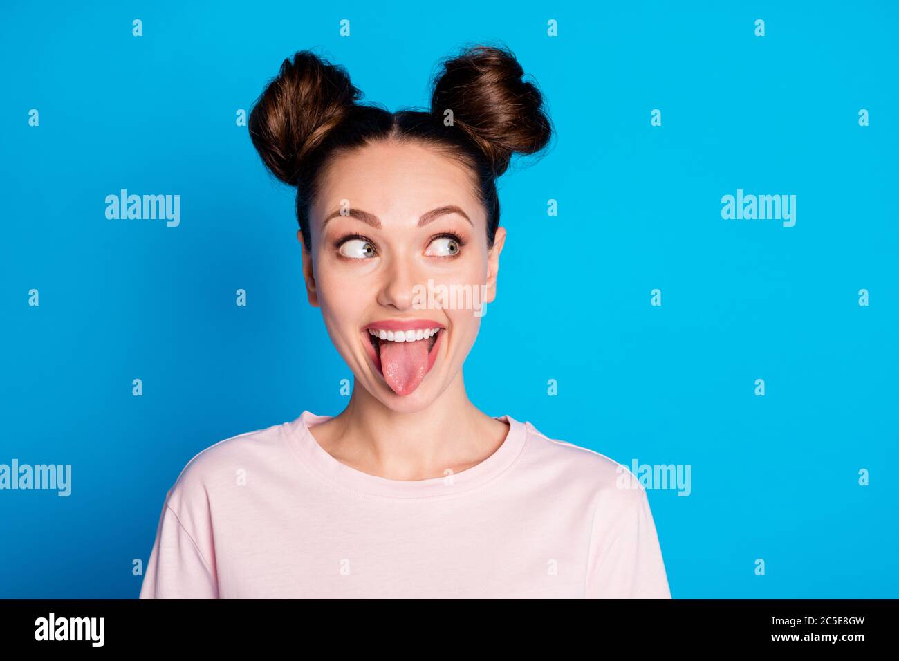 Closeup photo of attractive childish lady two funny buns stick tongue out mouth teasing boyfriend avoid look eyes bad behavior wear casual pink t Stock Photo