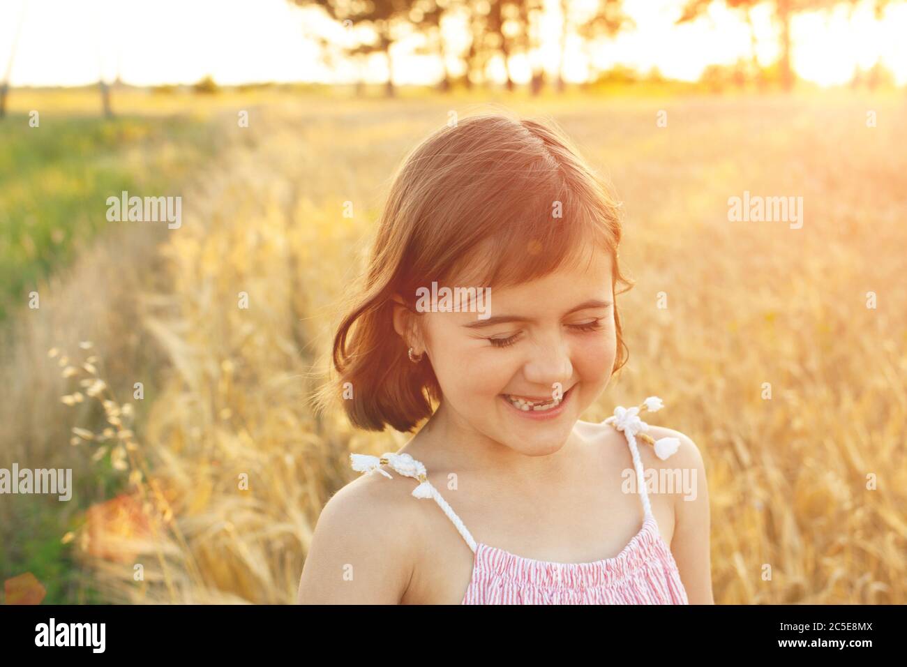 Funny girl laughs on a walk across the field at sunset. The concept of real childhood, digital detox, summer vacations, happiness. Stock Photo