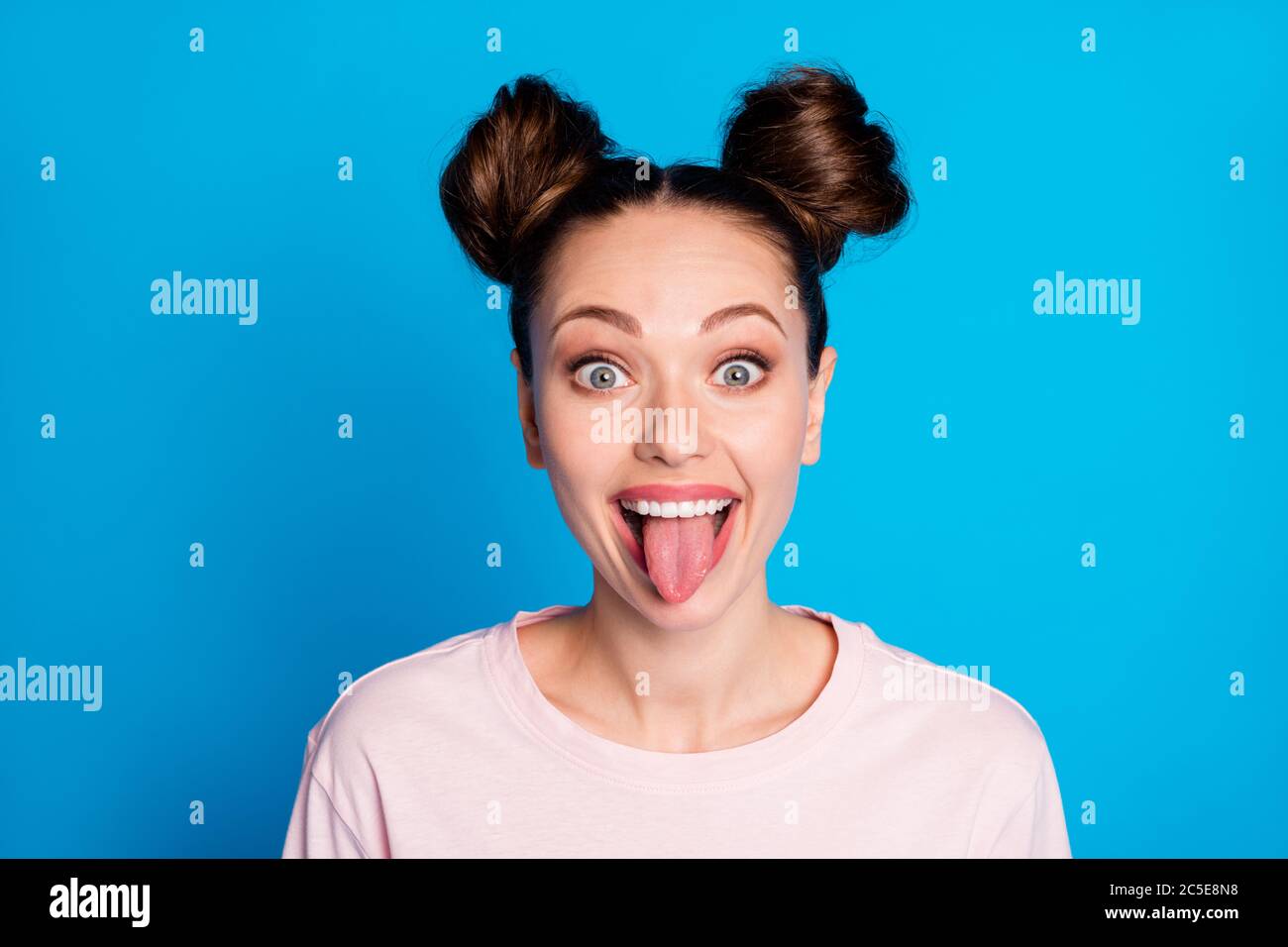 Closeup photo of attractive childish lady two funny buns sticking tongue out mouth teasing classmate bad behavior wear casual white pink t-shirt Stock Photo
