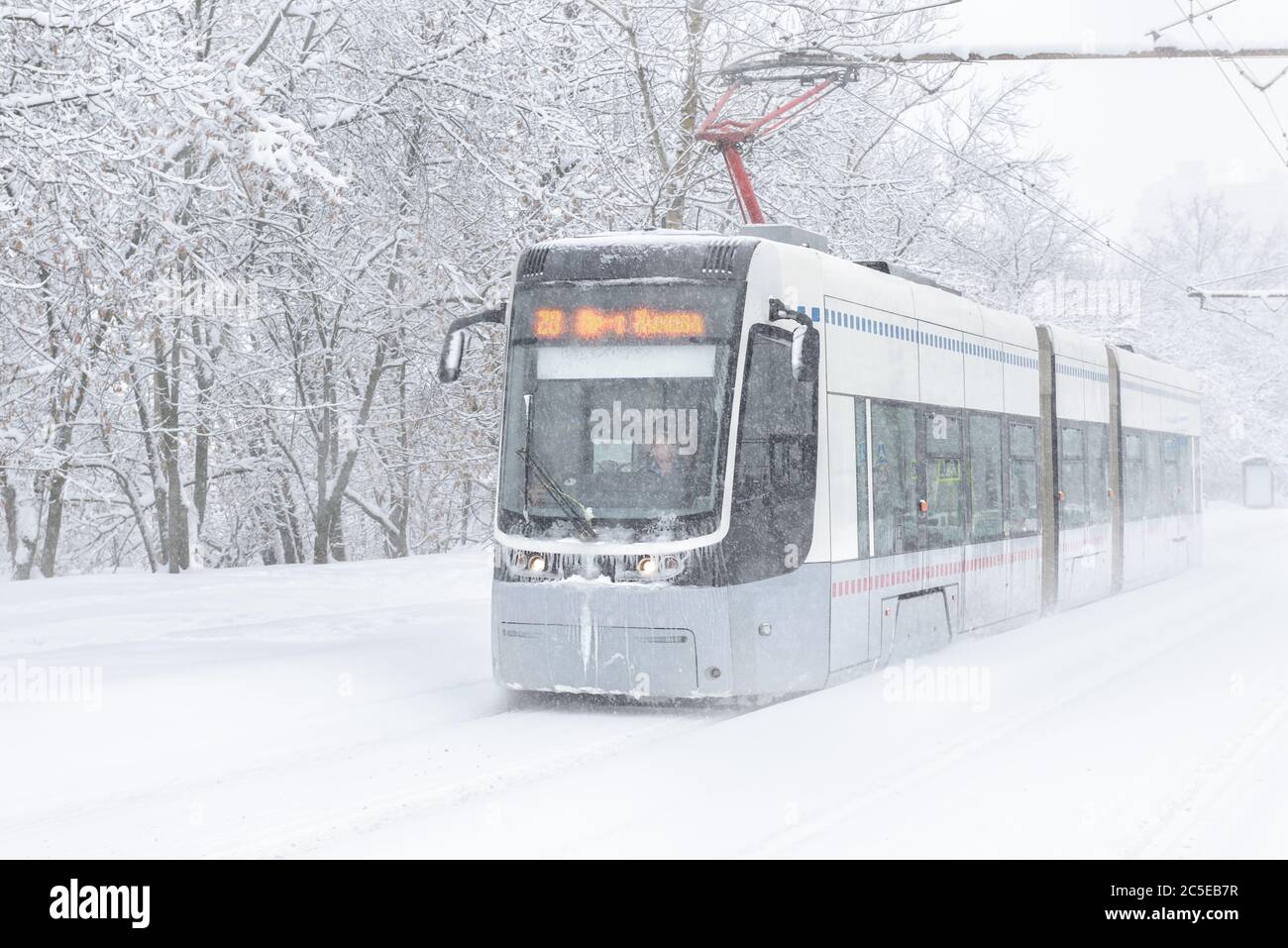 Tram goes along the street during snowstorm at winter in Moscow, Russia. Cold and snowfall in Moscow. Icy tram in snowy Moscow. Traditional view of Mo Stock Photo