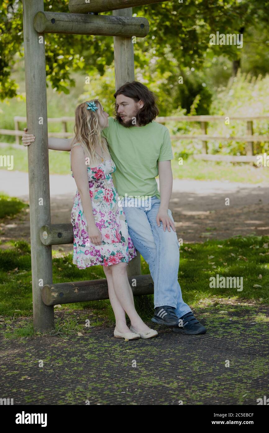 Young lovers sitting in the shade under tree in park on a sunny summer day, Springfield Park, London, model releases available Stock Photo