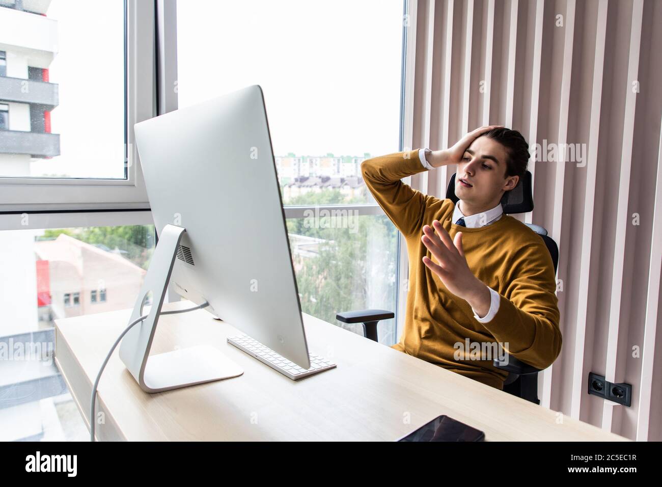 Frustrated businessman sitting on desk with hand on head in office Stock Photo