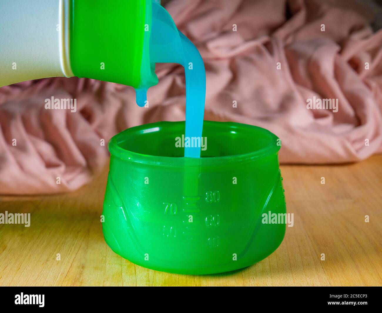Closeup of liquid gel detergent pouring from the spout of a plastic bottle  into a measuring cup, with dirty washing / laundry in the background Stock  Photo - Alamy