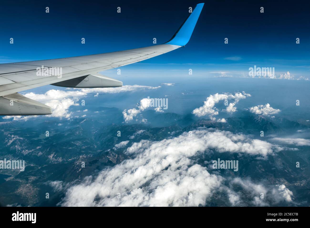 Wing of an airplane flying above clouds. The plane's wing on the blue sky and earth background. Panoramic aerial view of mountains from airplane windo Stock Photo