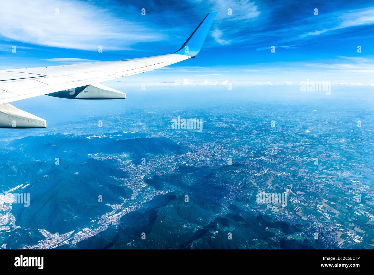 Wing of airplane flying above European mountains. Flight over Alps. The plane's wing on blue sky and earth background. Aerial panoramic view of land f Stock Photo