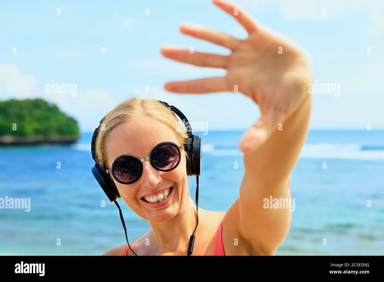 Young positive girl in headphones and sunglasses listening music and dancing with fun at tropical beach party. Travel family lifestyle, recreation Stock Photo