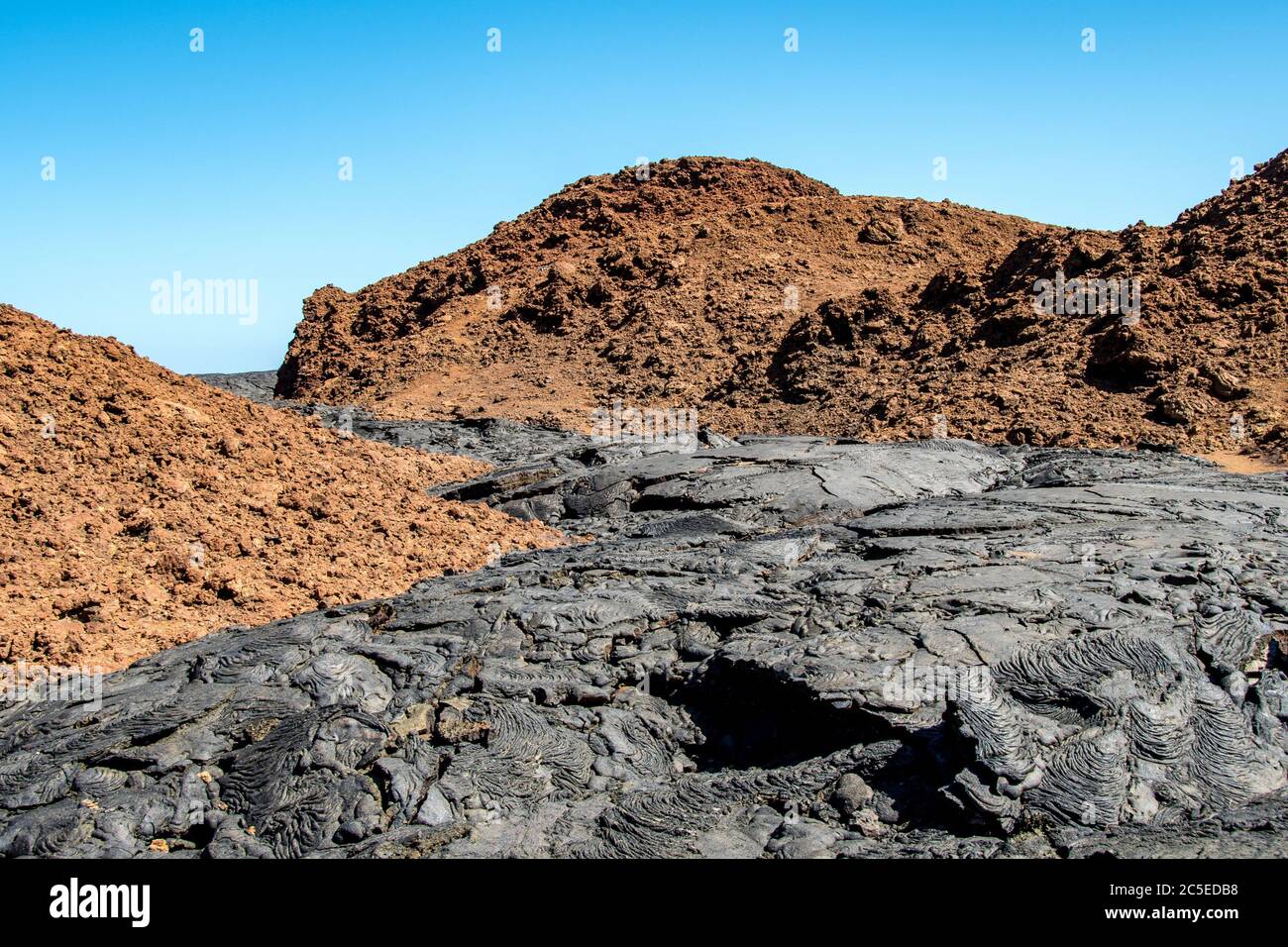 The flow of smooth and billowy black basaltic lava contrasts with the red of the oldest rocks of Santiago Island, Galapagos Stock Photo