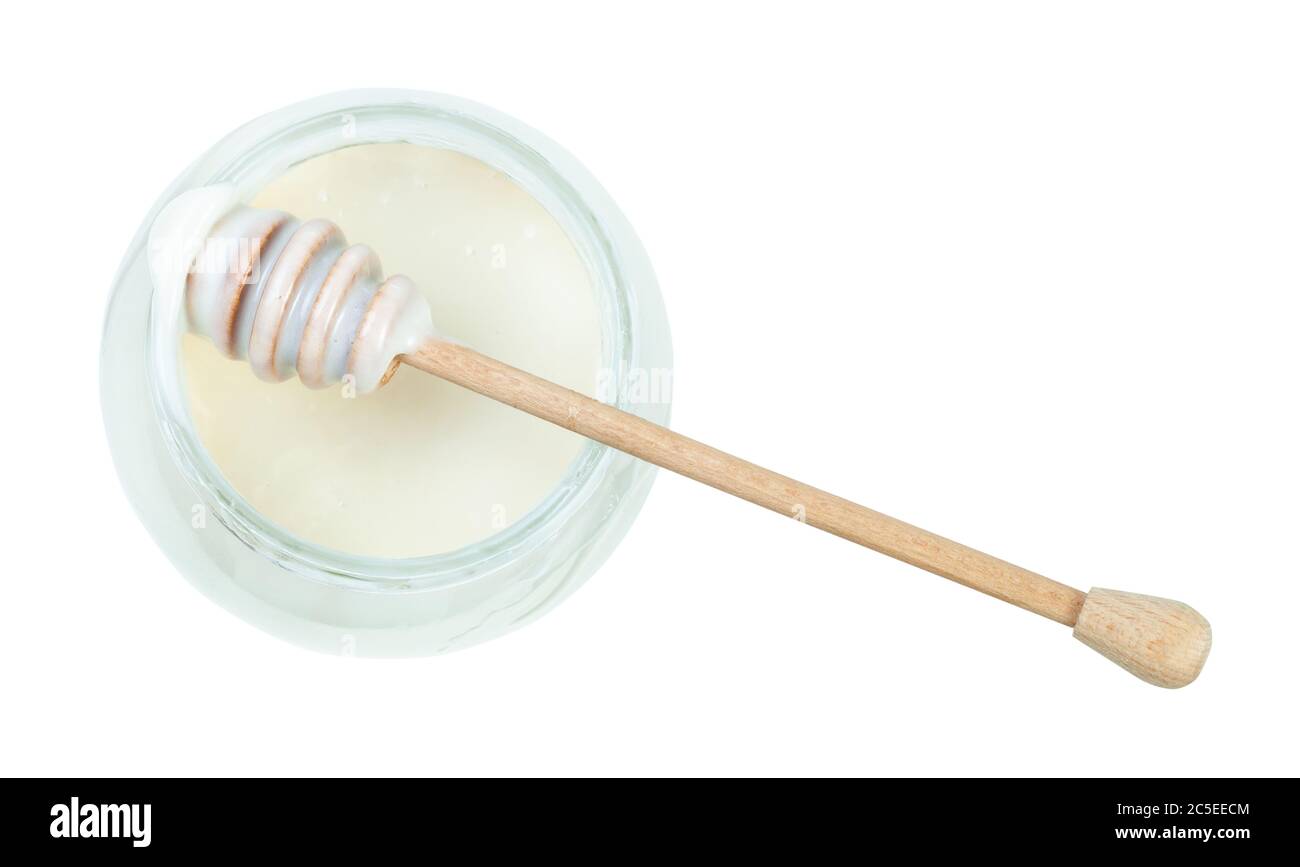 top view of wooden stick over glass jar with natural organic white honey isolated on white background Stock Photo