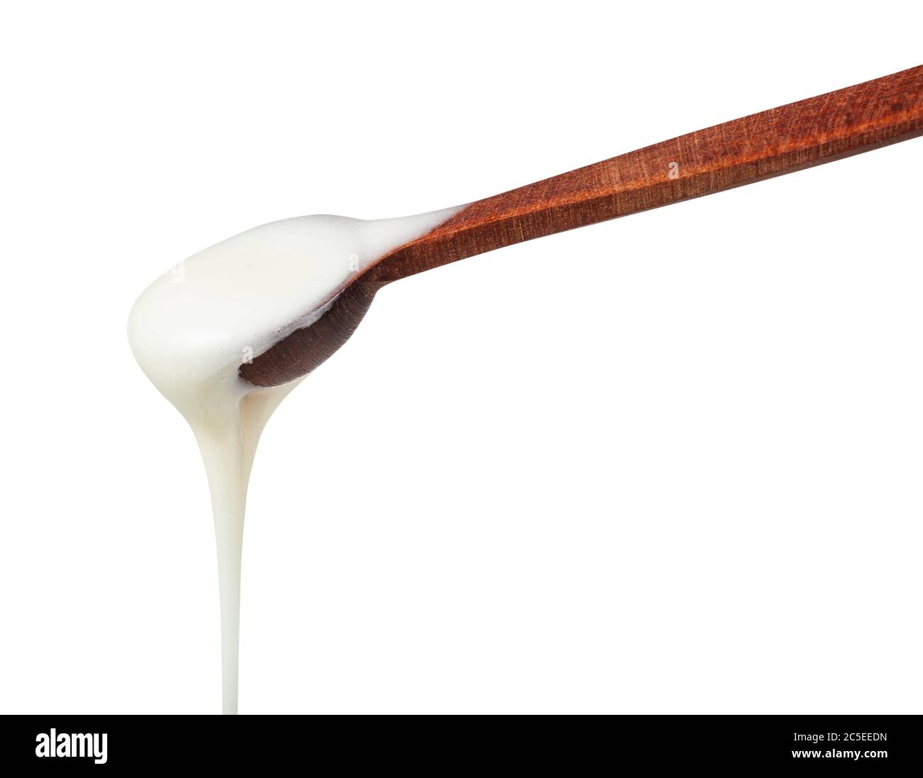 side view of natural organic white honey pouring from little wooden spoon closeup isolated on white background Stock Photo