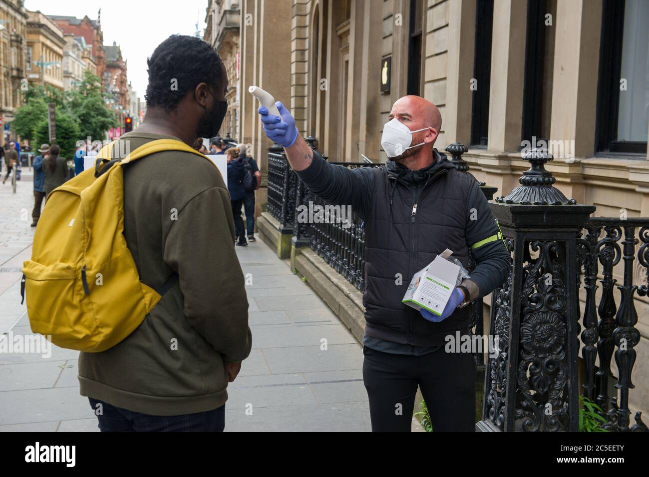 Glasgow, Scotland, UK. 2nd July, 2020. Pictured: An employee takes customers temperature before being allowed into the Apple Shop. Scenes from Glasgows style mile, Buchanan Street shopping area, where more people are seen wearing face masks or home made face coverings. Nicola Sturgeon announced earlier today that wearing a face covering is to become mandatory in shops from 10th July next week. Face coverings are already mandatory when taking public transport in a bid to slow down the spread of coronavirus. Credit: Colin Fisher/Alamy Live News Stock Photo