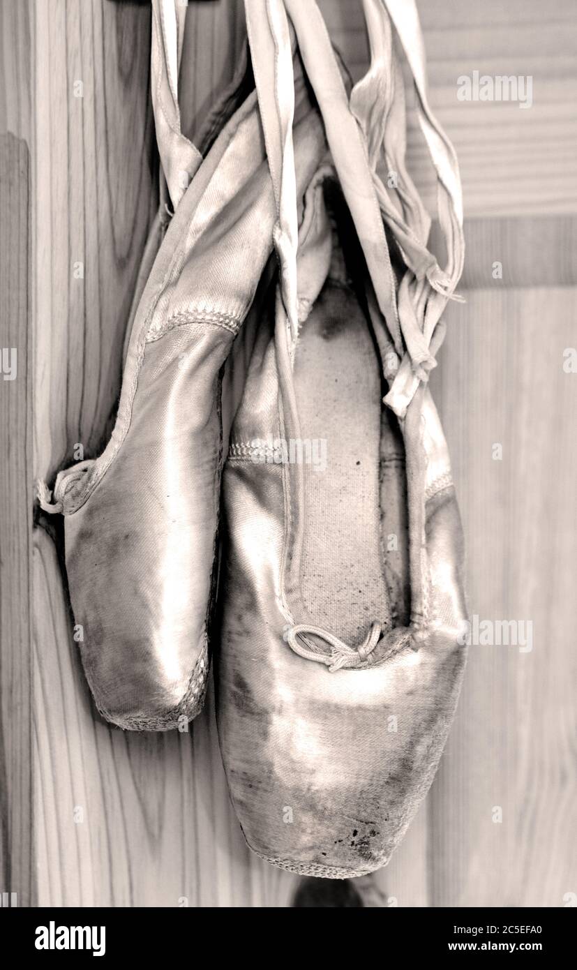 A pair of worn out ballet shoes hanging by the ribbons. Stock Photo