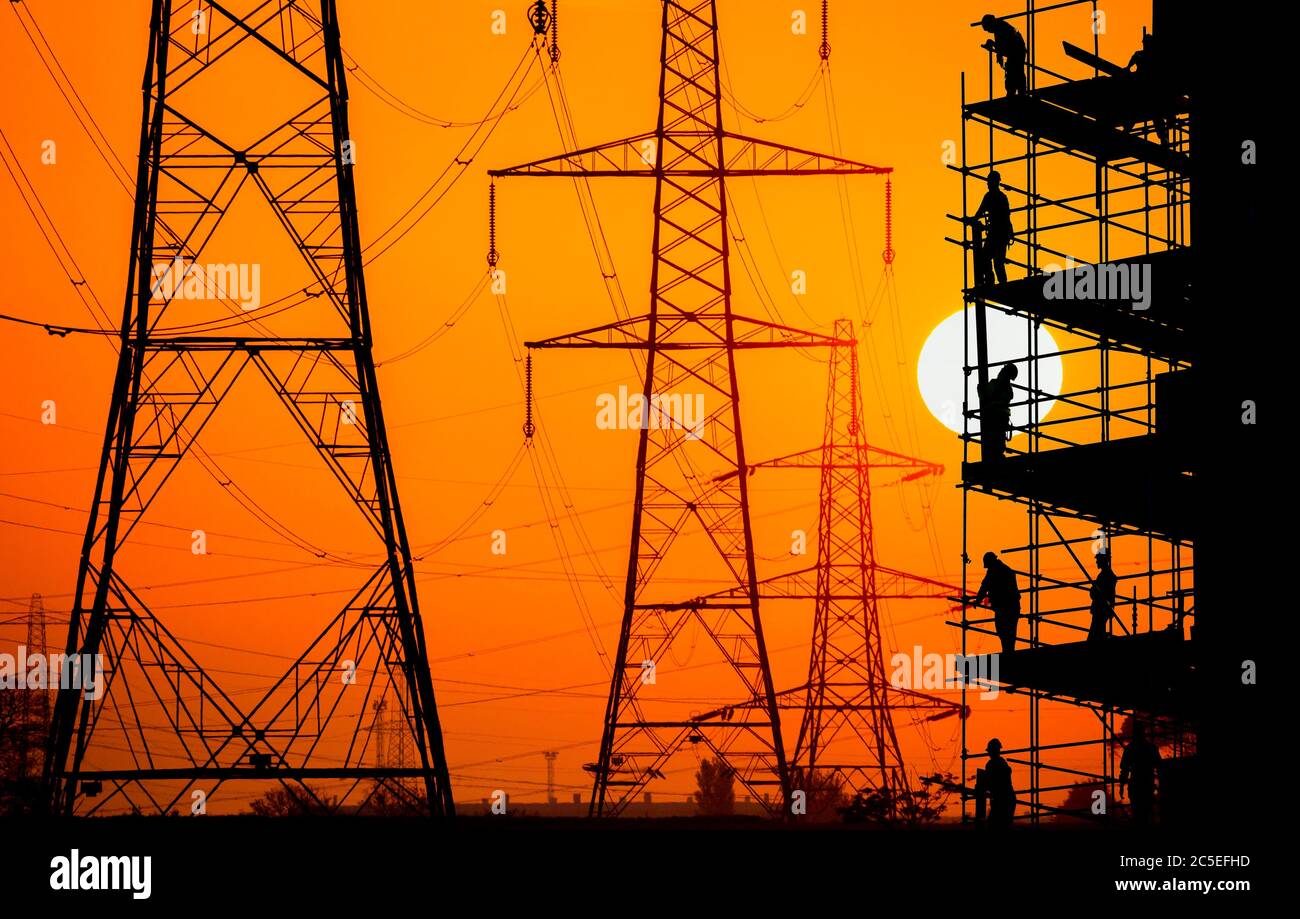 Construction/building workers on scaffolding with electricity pylons at sunrise overlayed, UK. Concept image: building industry, energy, employment. Stock Photo