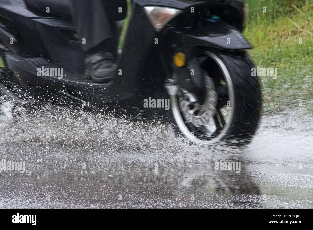 Motorcycle moped rides through a puddle on a wet road in the rain