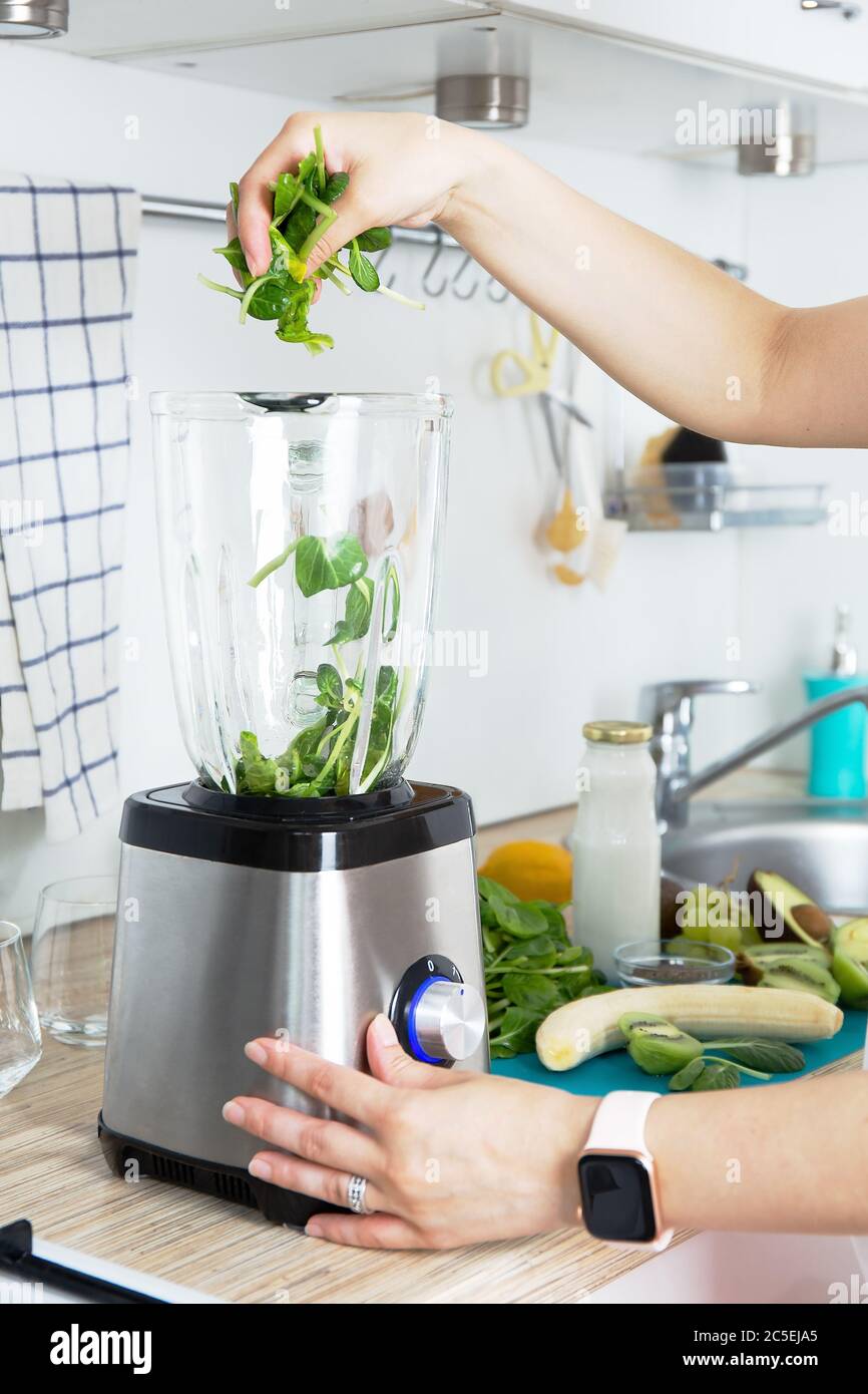 Girl hands prepare a green smoothie, puts fresh spinach leaves in a blender. Healthy eating concept. Vegetarianism, vegan food, fitness food, detox Stock Photo