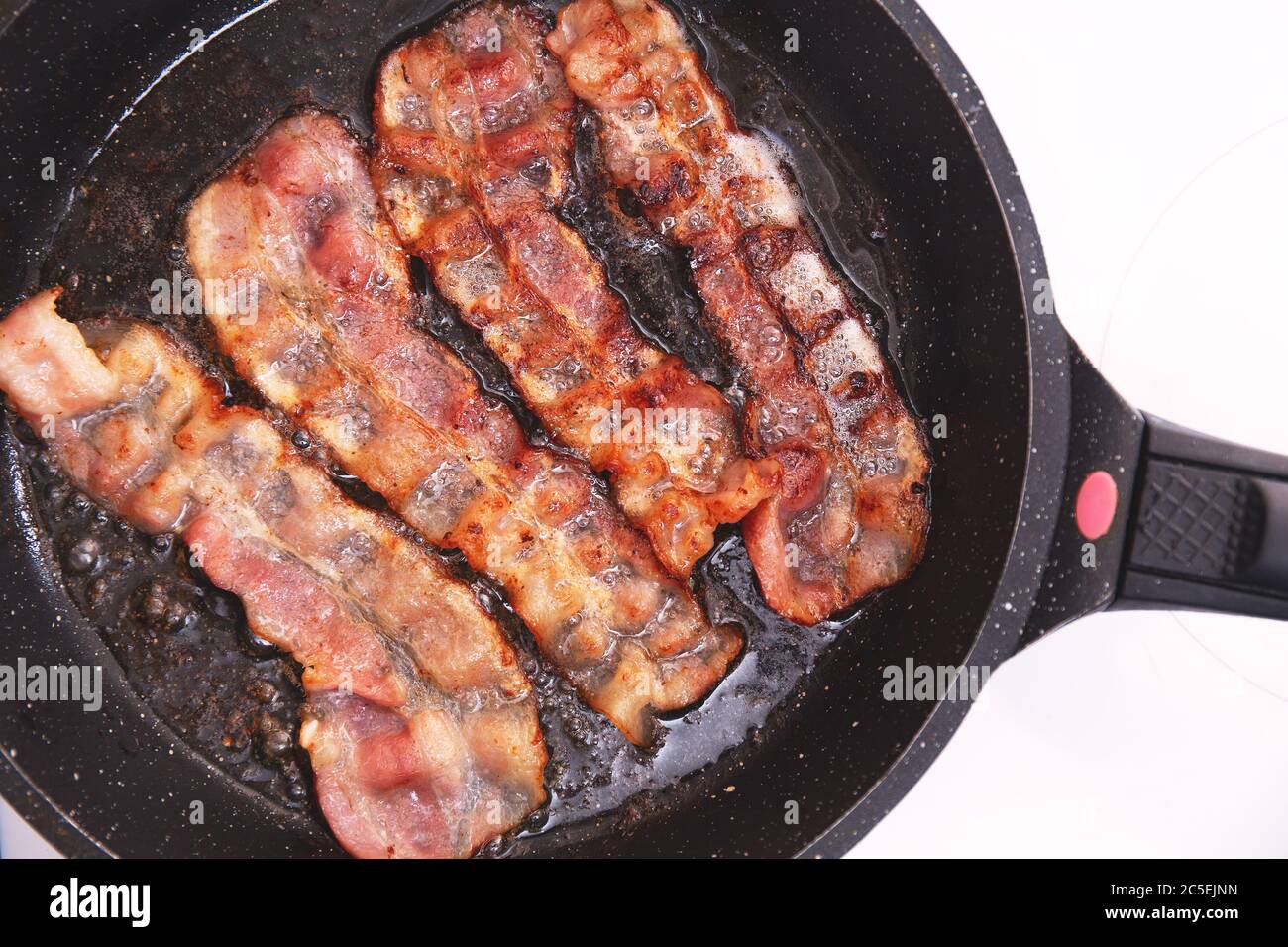 Bacon strips or rashers being cooked in frying pan. Hearty highcalorie breakfast. Fast food