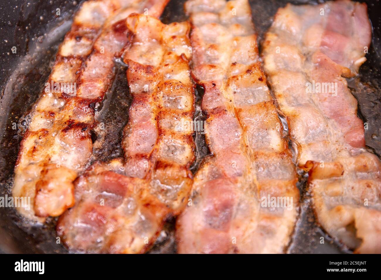 Bacon strips or rashers being cooked in frying pan. Hearty highcalorie