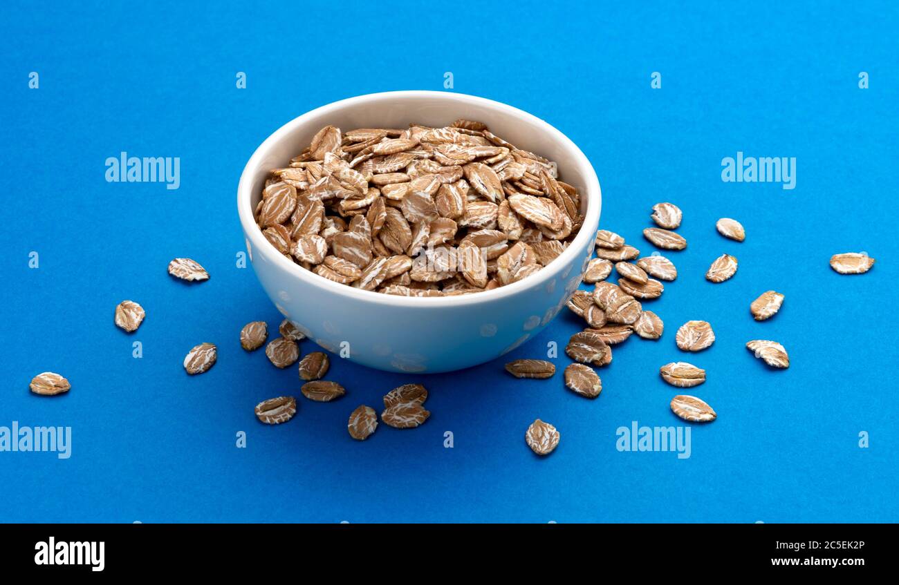 Oat rye flakes in bowl isolated on blue color background Stock Photo