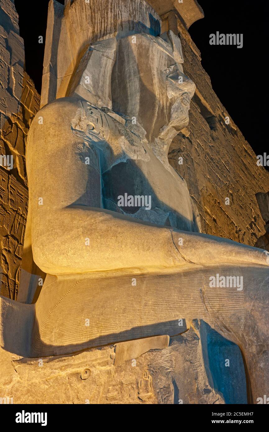 Large statue of Ramses II at entrance pylon to ancient egyptian Luxor Temple lit up during night Stock Photo
