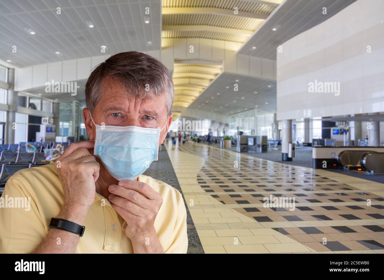 Senior man or traveler adjusting face mask in airport terminal and looking afraid of travel with coronavirus Stock Photo