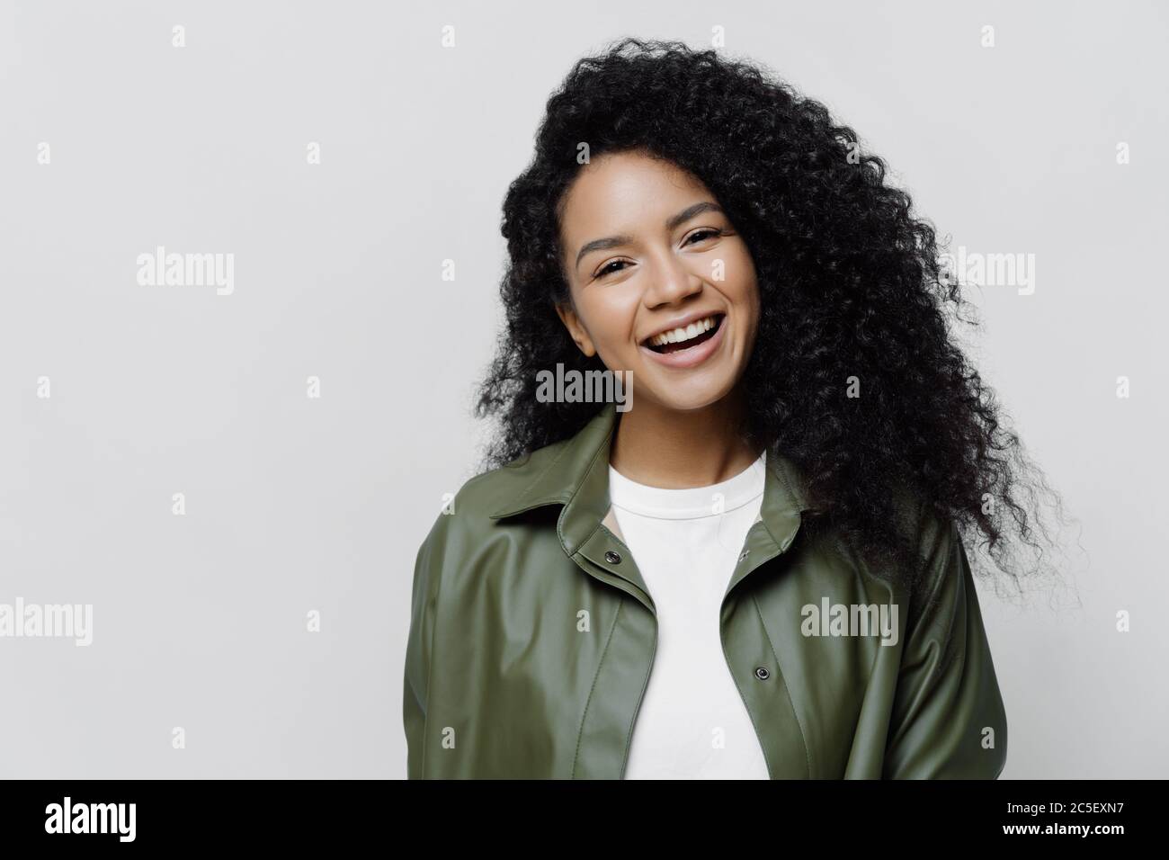 Portrait of carefree joyful African American lady with beaming smile and curly bushy hair, glad to be promoted at work, hears excellent news, dressed Stock Photo