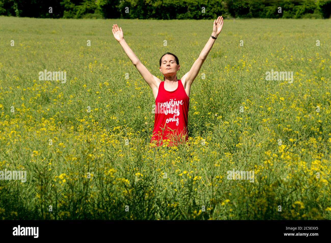 A young woman in a red tee shirt arms raised up to the sky, celebrating freedom. Positive vibes only written on the T shirt Stock Photo