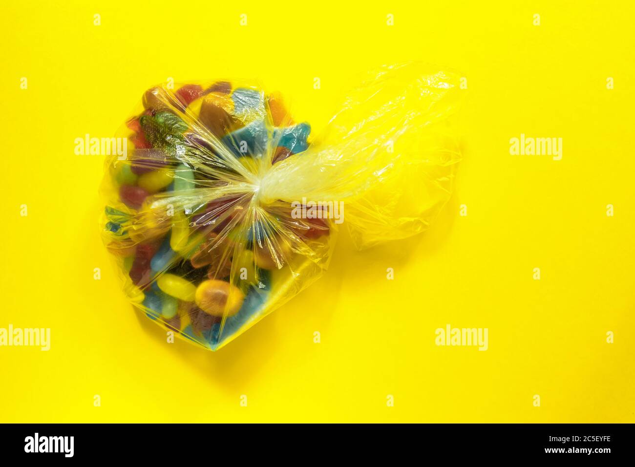 Multi-colored glazed jelly beans sweets in plastic package on yellow paper background. Stock Photo