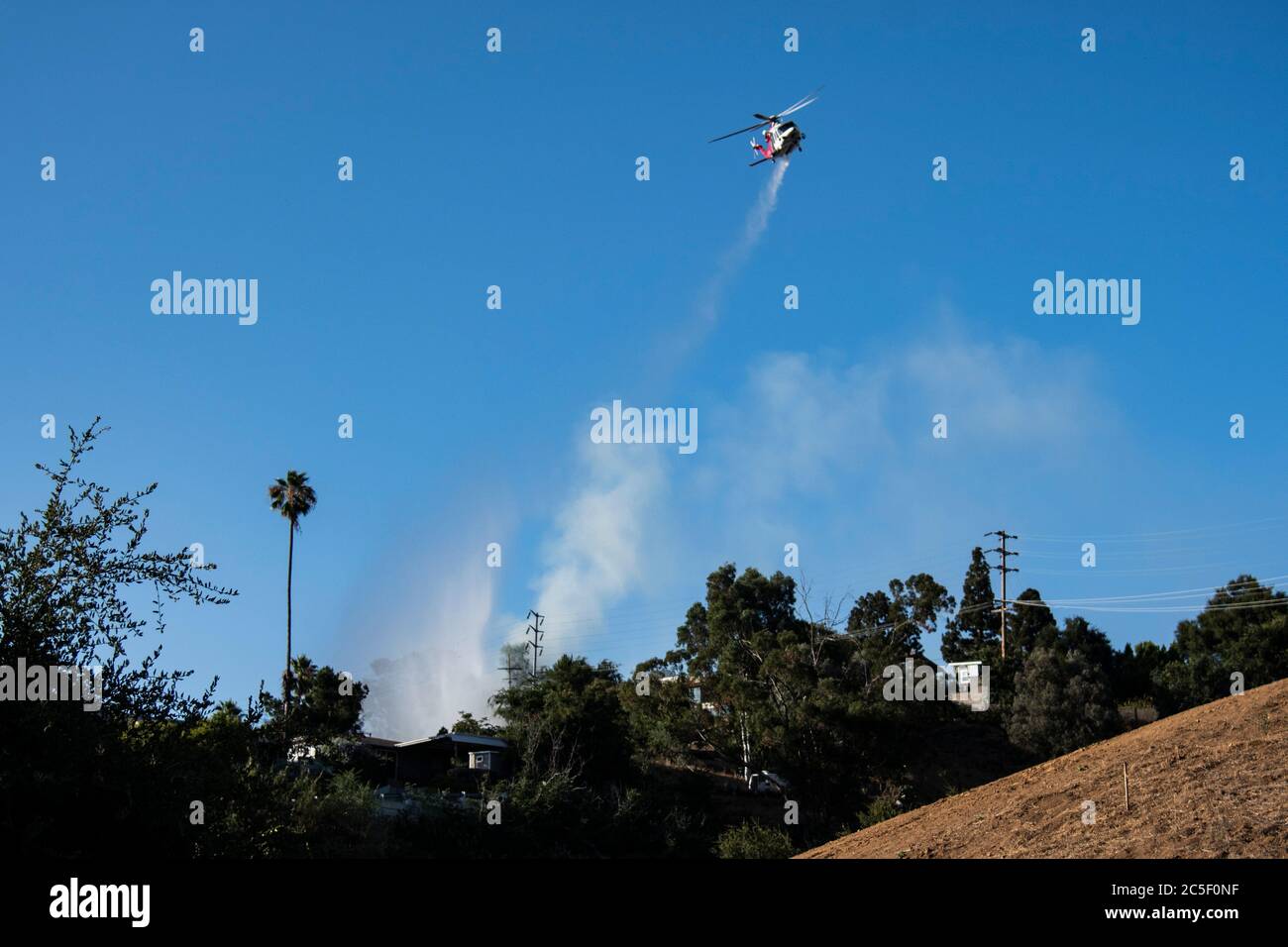 Emergency firefighting helicopter drops water on a brush fire saving homes in a California wild fire. Stock Photo