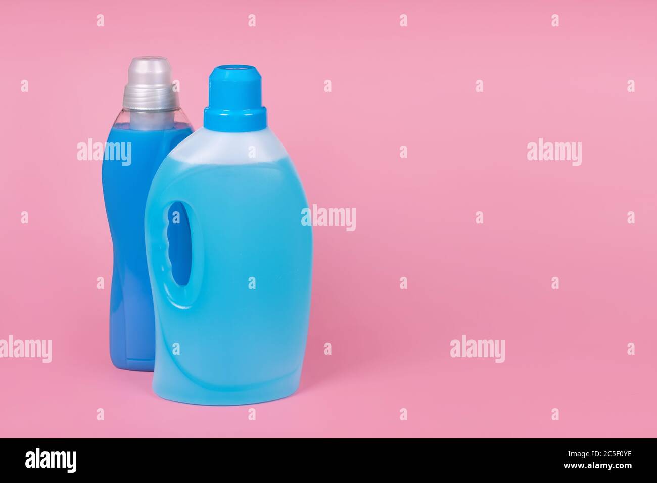 Bottles of detergent and fabric softener on pink background. Containers of cleaning products, household chemicals. Liquid laundry detergent and Stock Photo