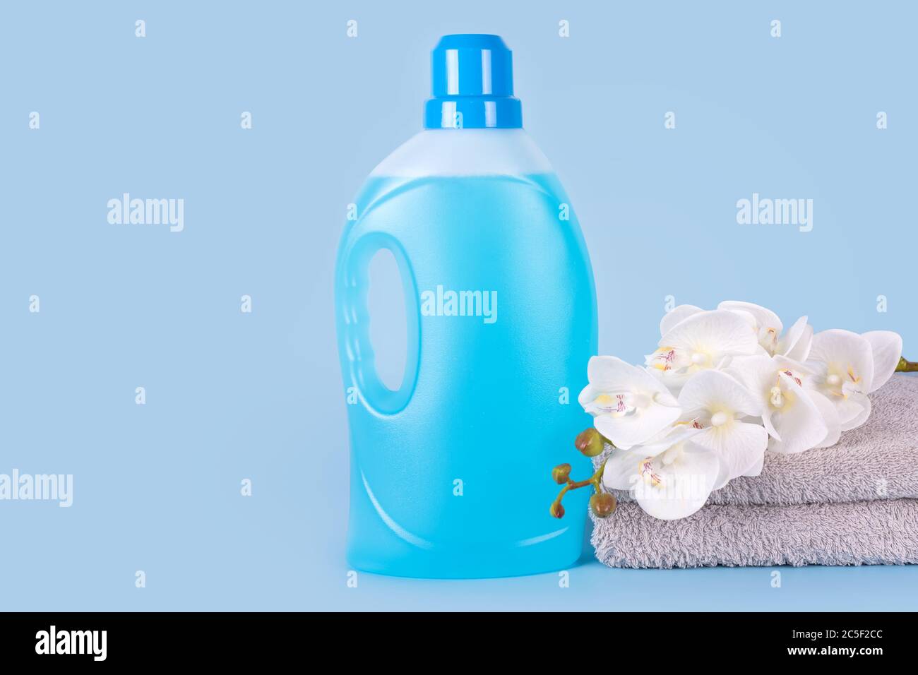 Bottle of detergent with clean towels and flowers on blue background