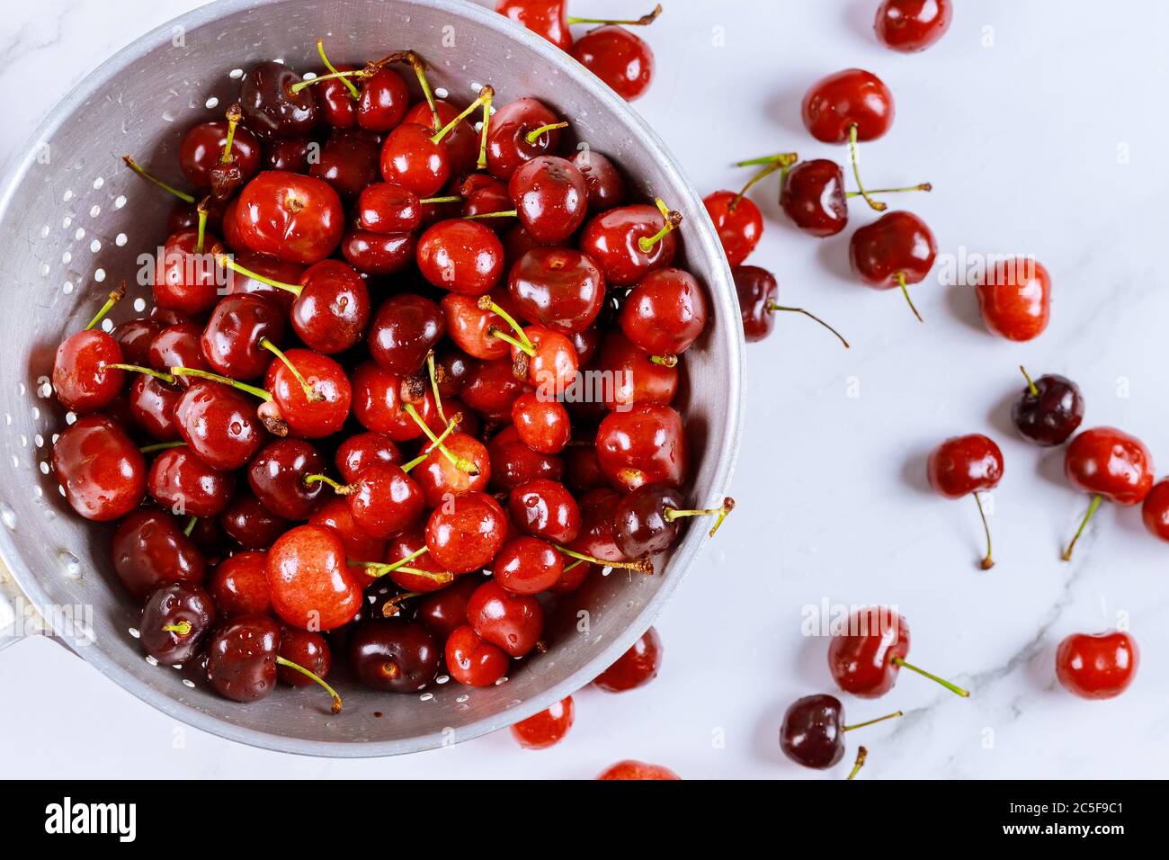 Berry cherries in colander bowl with water drops on white background. Top view. Stock Photo