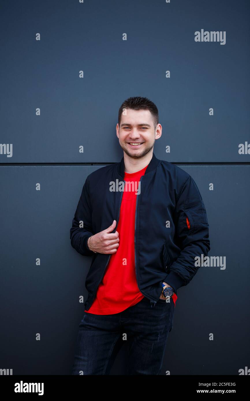 A young man dressed in urban style stands on the street against a gray ...