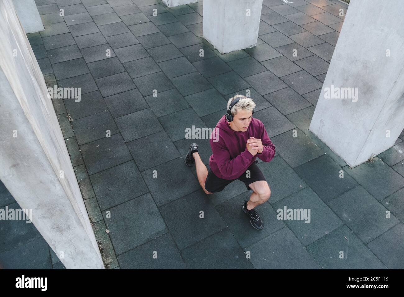Young athletic man with headphones listen to music and warming up outdoors. Do lunge Stock Photo