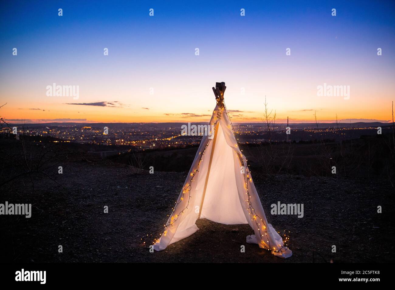 Teepee on top of hill with small chain light inside tent during sunset with view to landscape Stock Photo