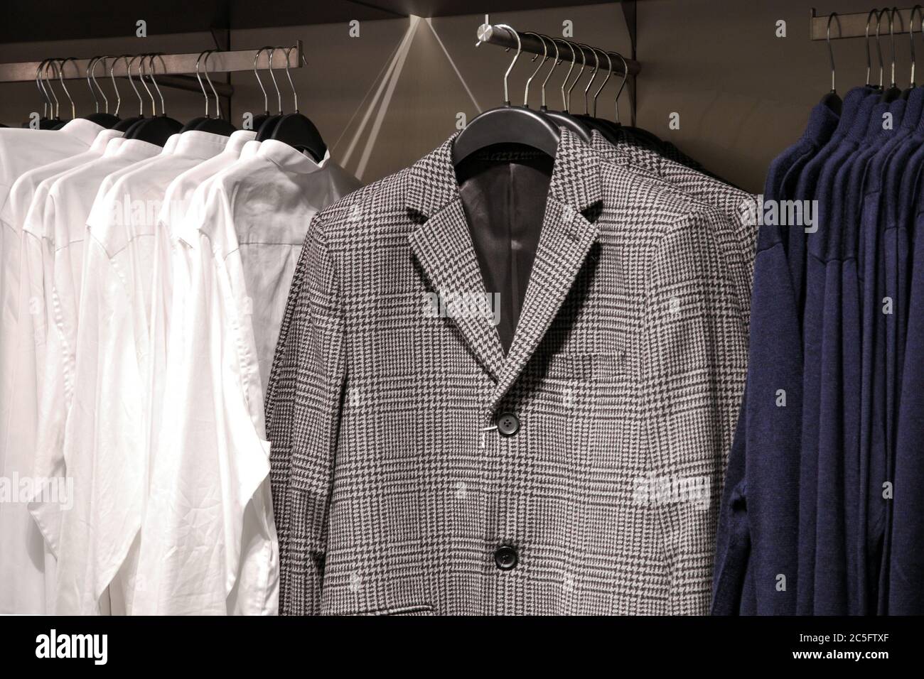 men's casual clothes in store, trendy jackets, shirts, cardigans on hangers Stock Photo