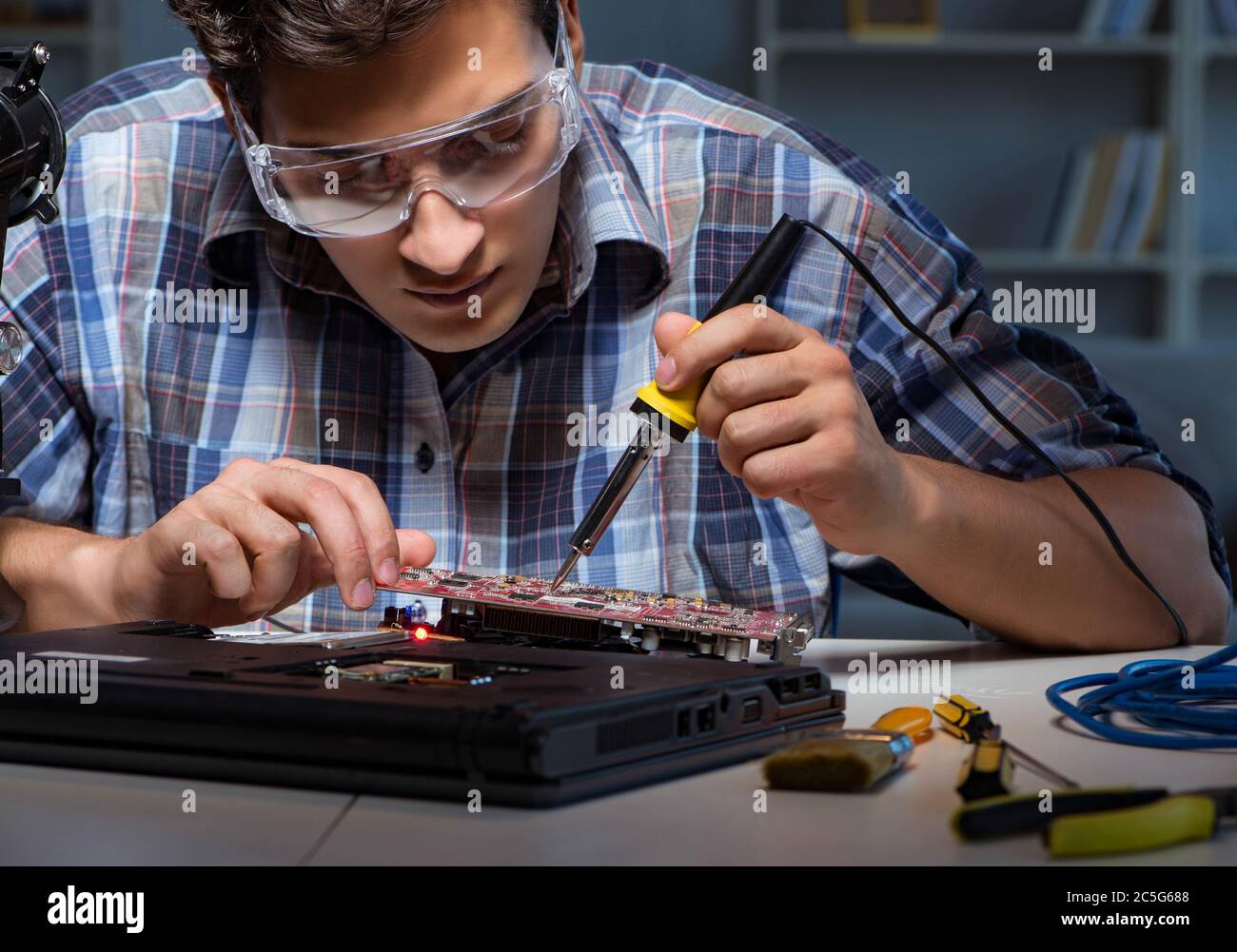 Young repair technician soldering electrical parts on motherboard Stock